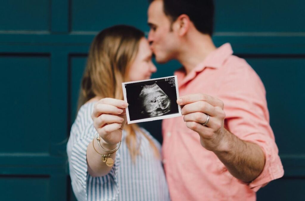 man kissing woman's forehead white holding ultrasound photo